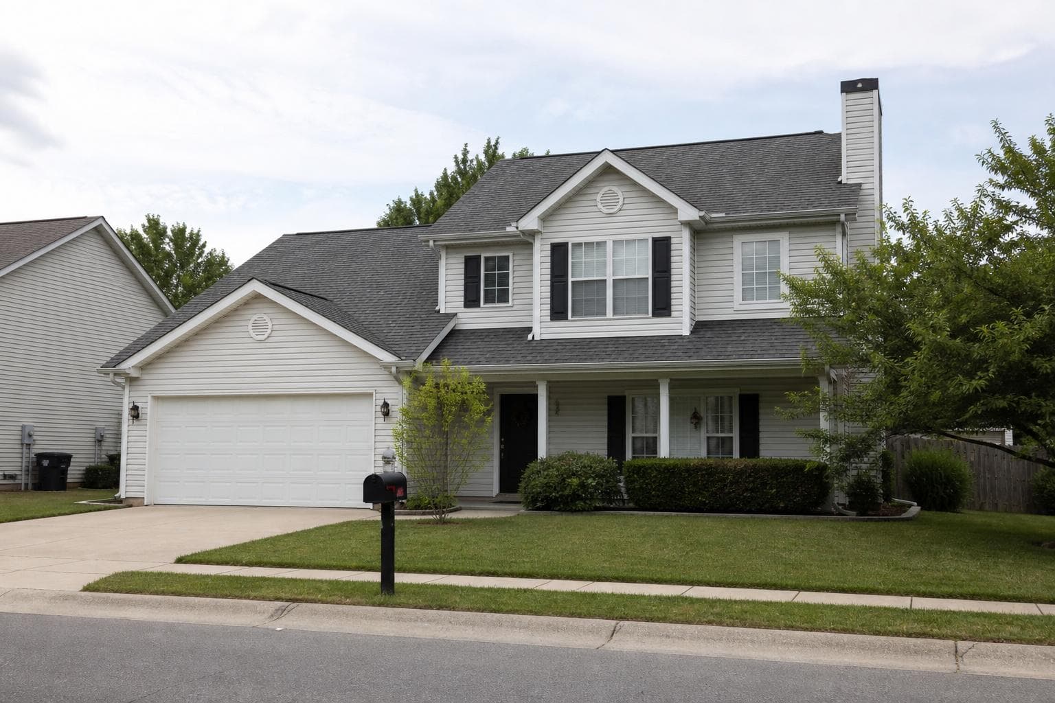 Typical two-story suburban house with a gray asphalt-shingle roof, vinyl siding, and a two-car garage