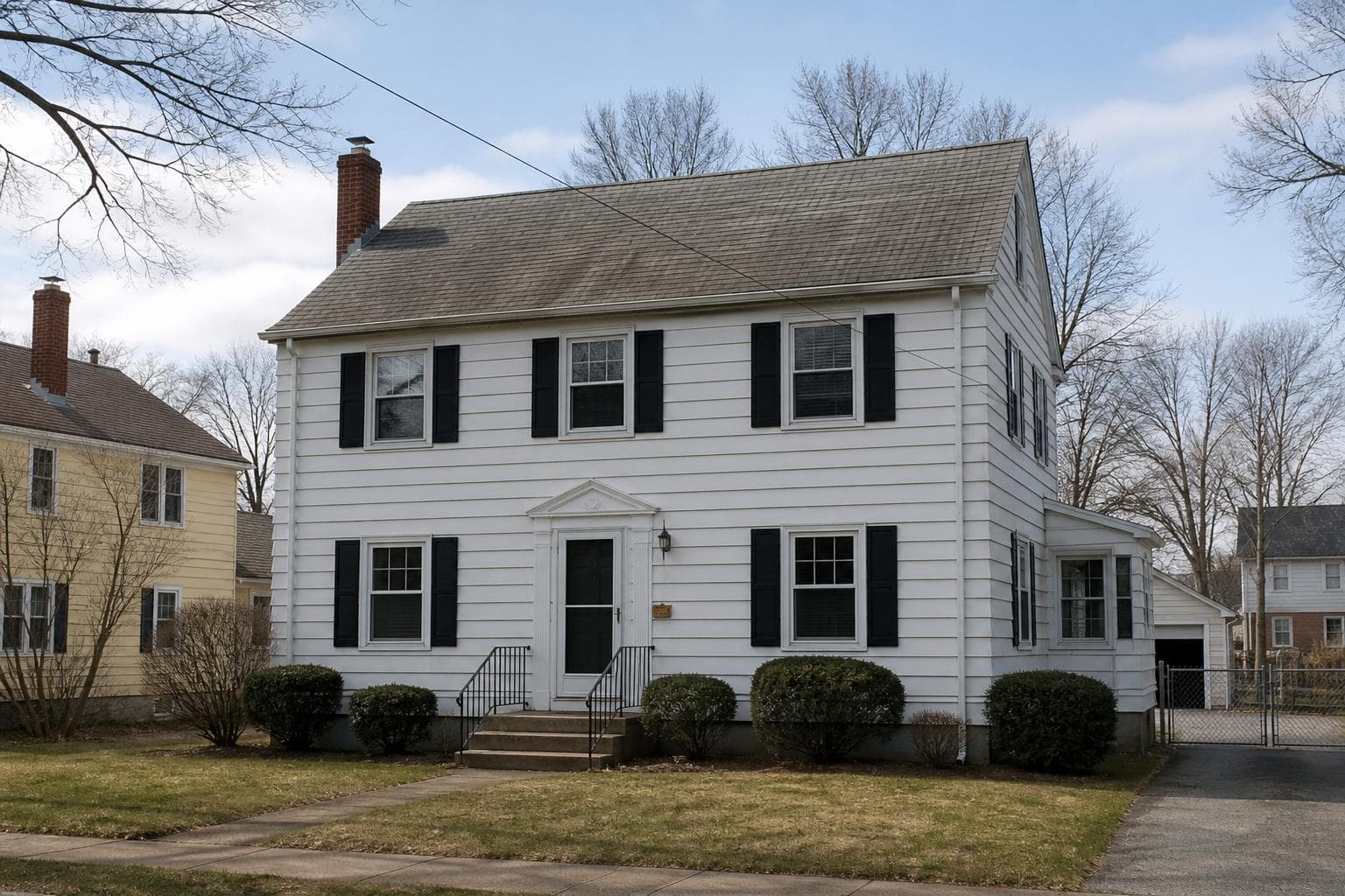 Classic two-story colonial with white siding, black shutters, and a weathered gray shingle roof